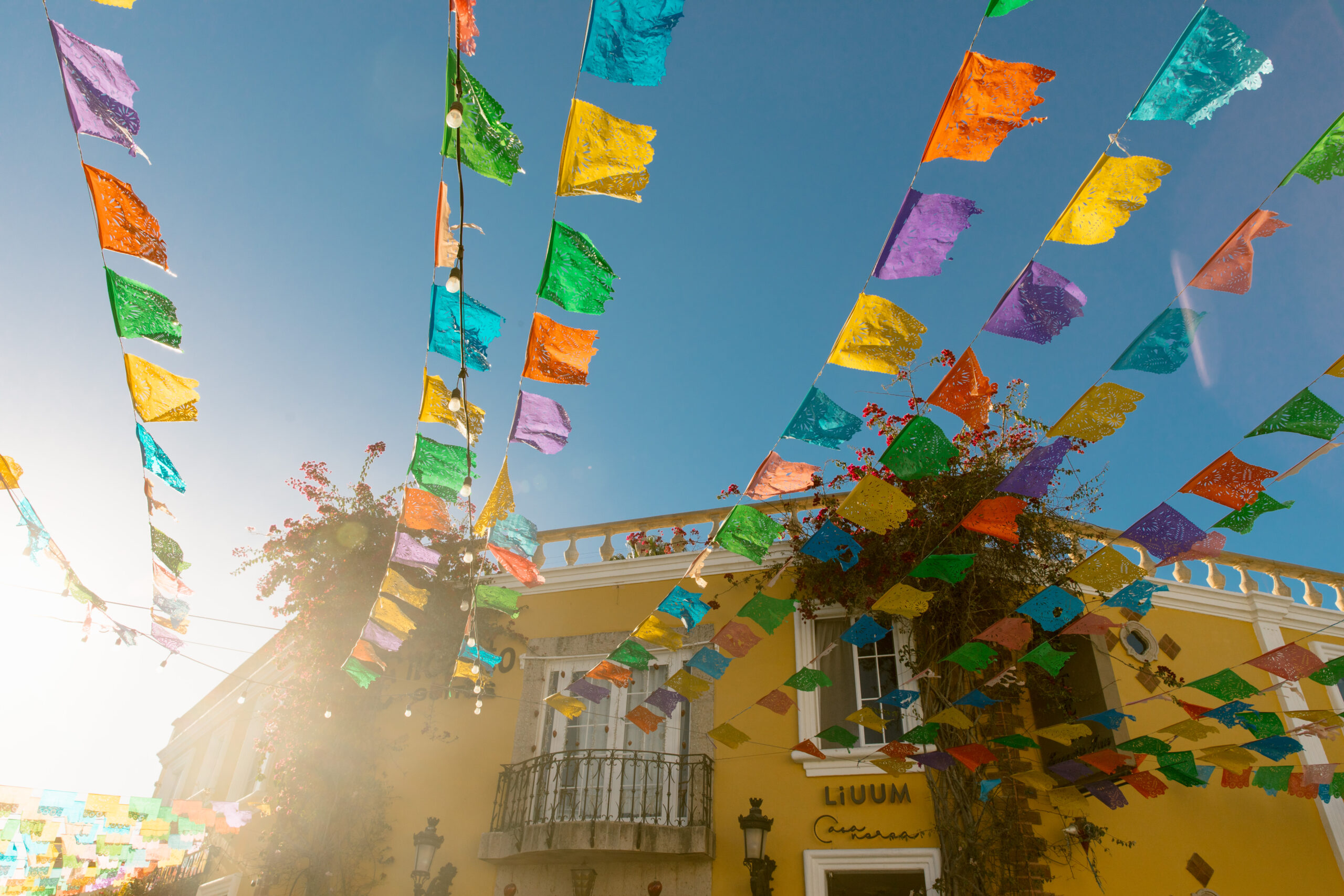 colorful papel picado banners blowing in wind blue skies Yellow LiUUM building. Downtown San Jose Del Cabo Mexican architecture