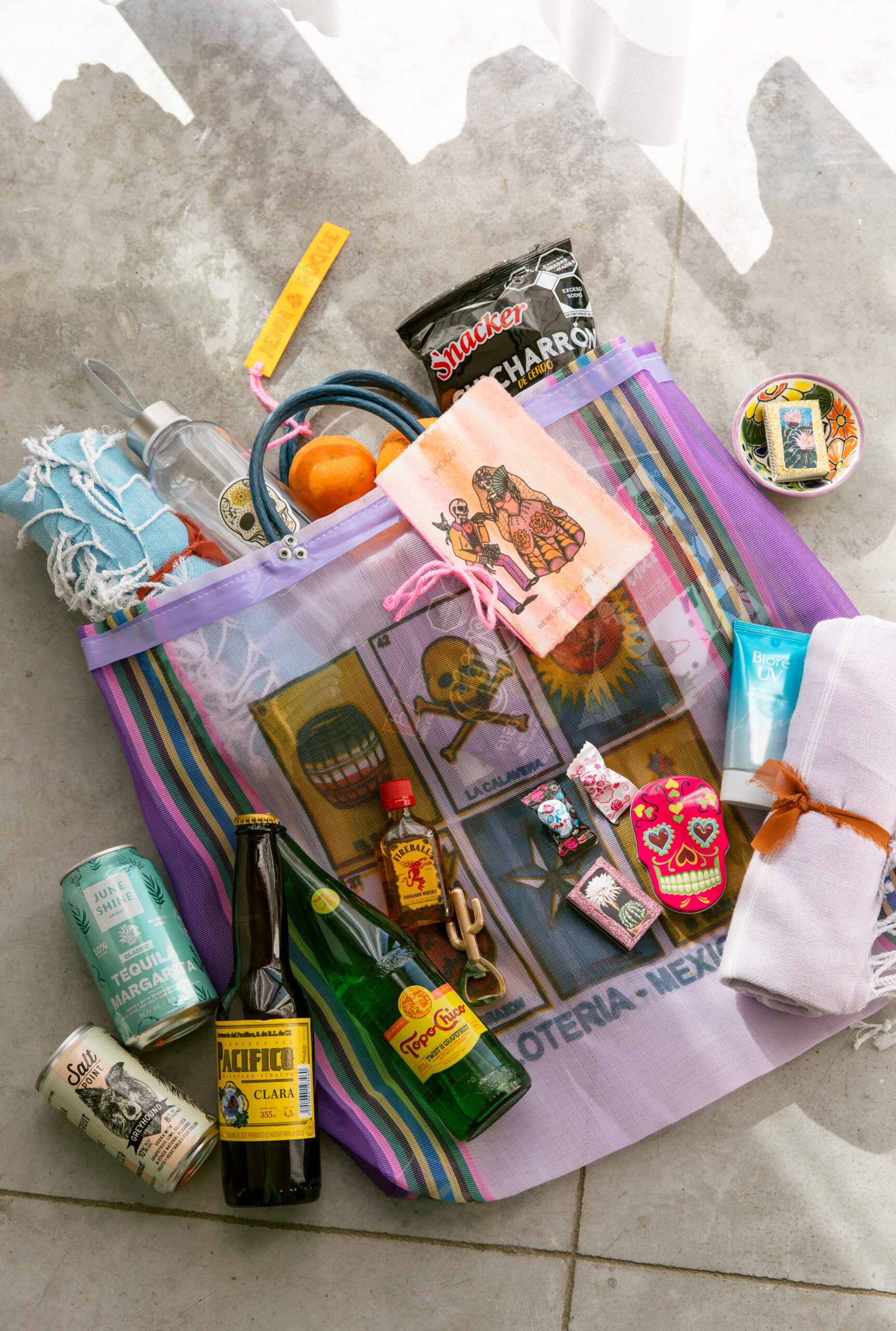 Colorful gift bags Mexican wedding. Purple loteria themed tote bag from Mexican art market. Locally sourced Mexican snacks. Handmade wedding itinerary. Topo chico. custom matches. Skull candies. beach towels. Reusable water bottle. hand crafted ceramic ash dish. Pacifico. Salt Point. Canned margarita. mini fireball. gold cactus bottle opener. 