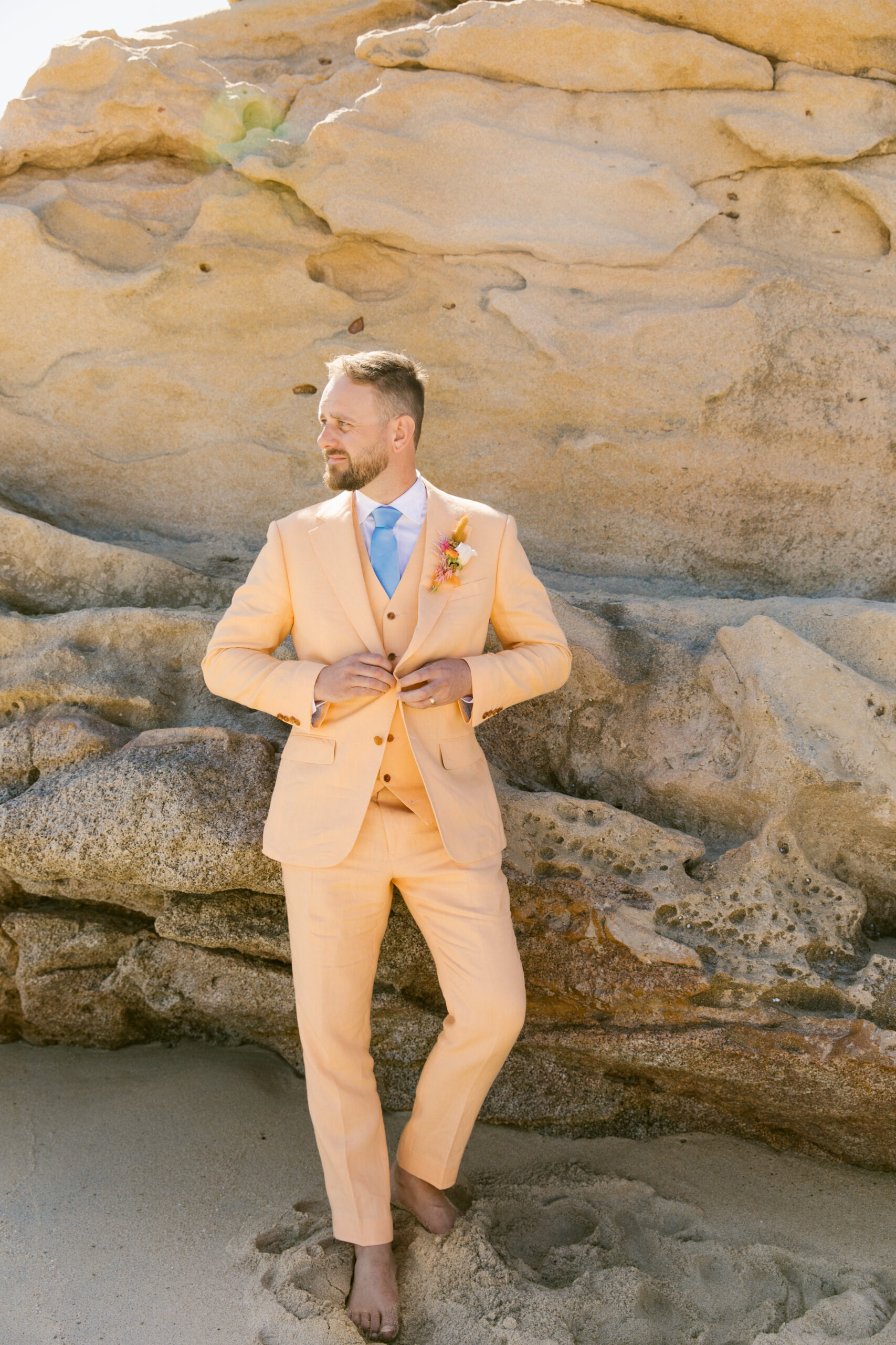 bright peach or coral linen suit cotswold tailors with pink orange and white boutenir. light blue tie with octopus tentacle tie clip. colorful groom style. 
groom portrait destination beach wedding in mexico