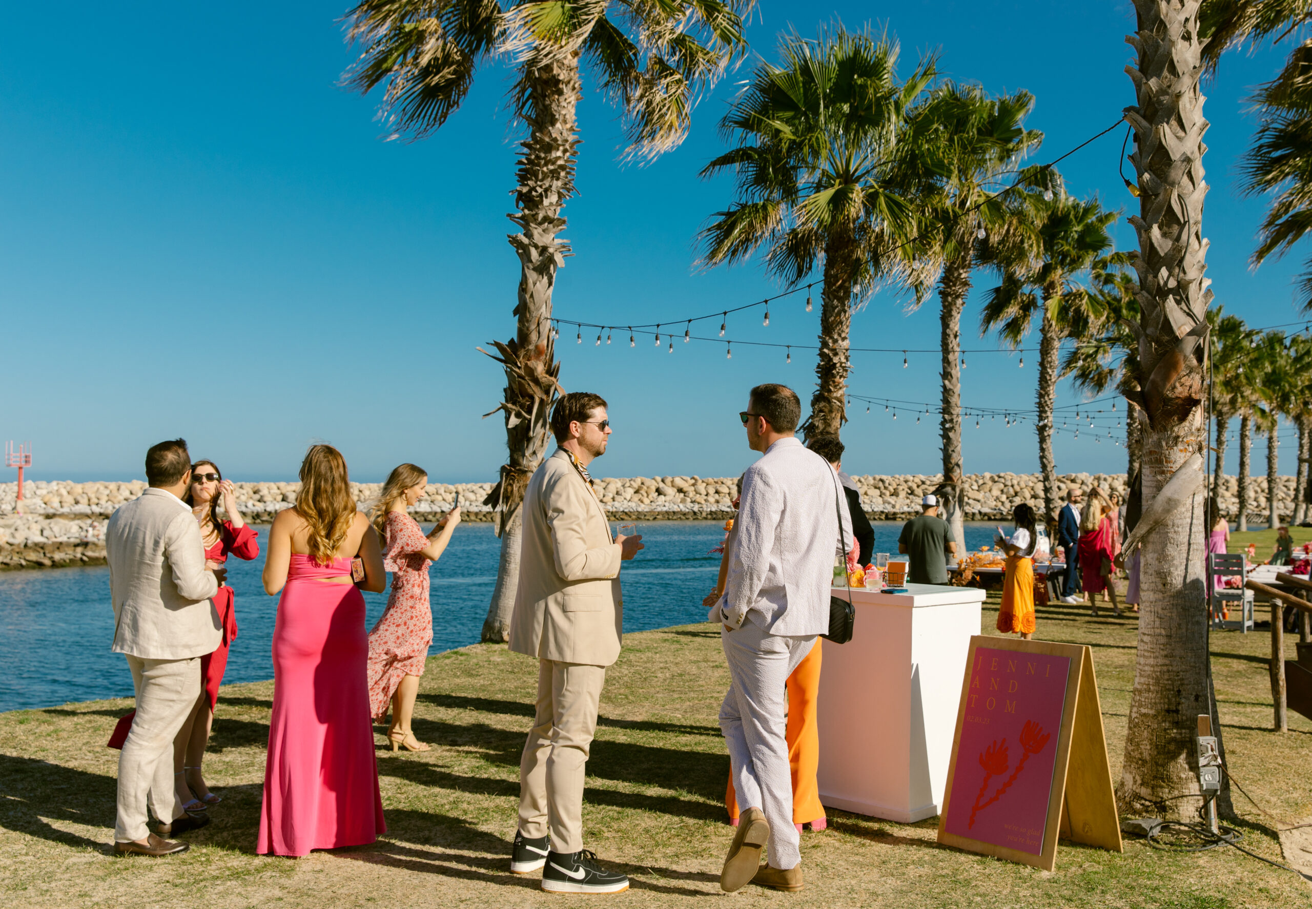 unique and colorful wedding ceremony florals. mexico wedding ceremony on jetti at beach club. ocean beach view in the background. palm trees white sand beaches. blue clear ocean water. blue skies. palm tree runway. colorful wedding guest attire. custom colorful wedding welcome sign pink orange and yellow