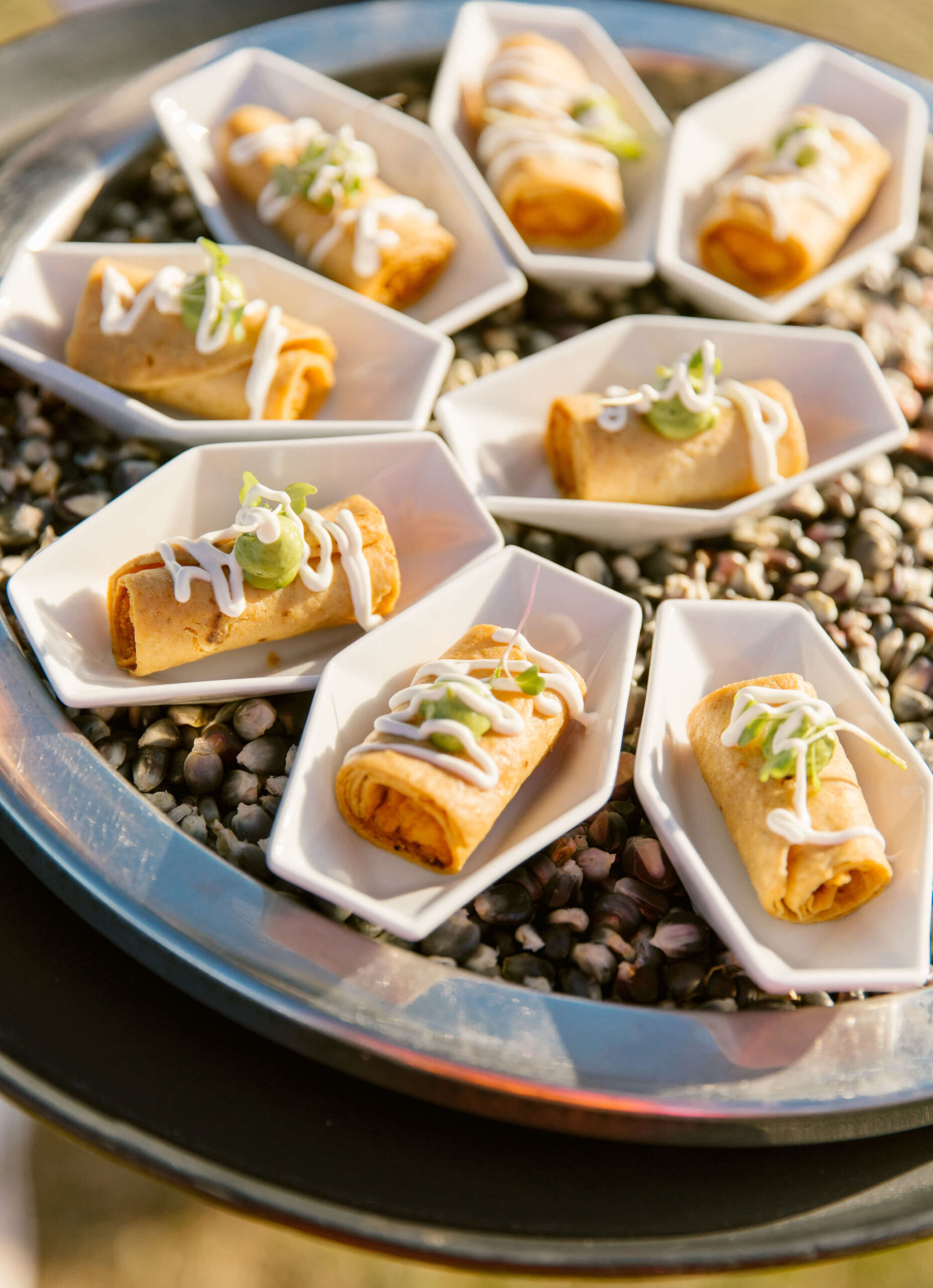 wedding cocktail hour appetizer. mini taquitos with crema and guacamole on tray of pebbles