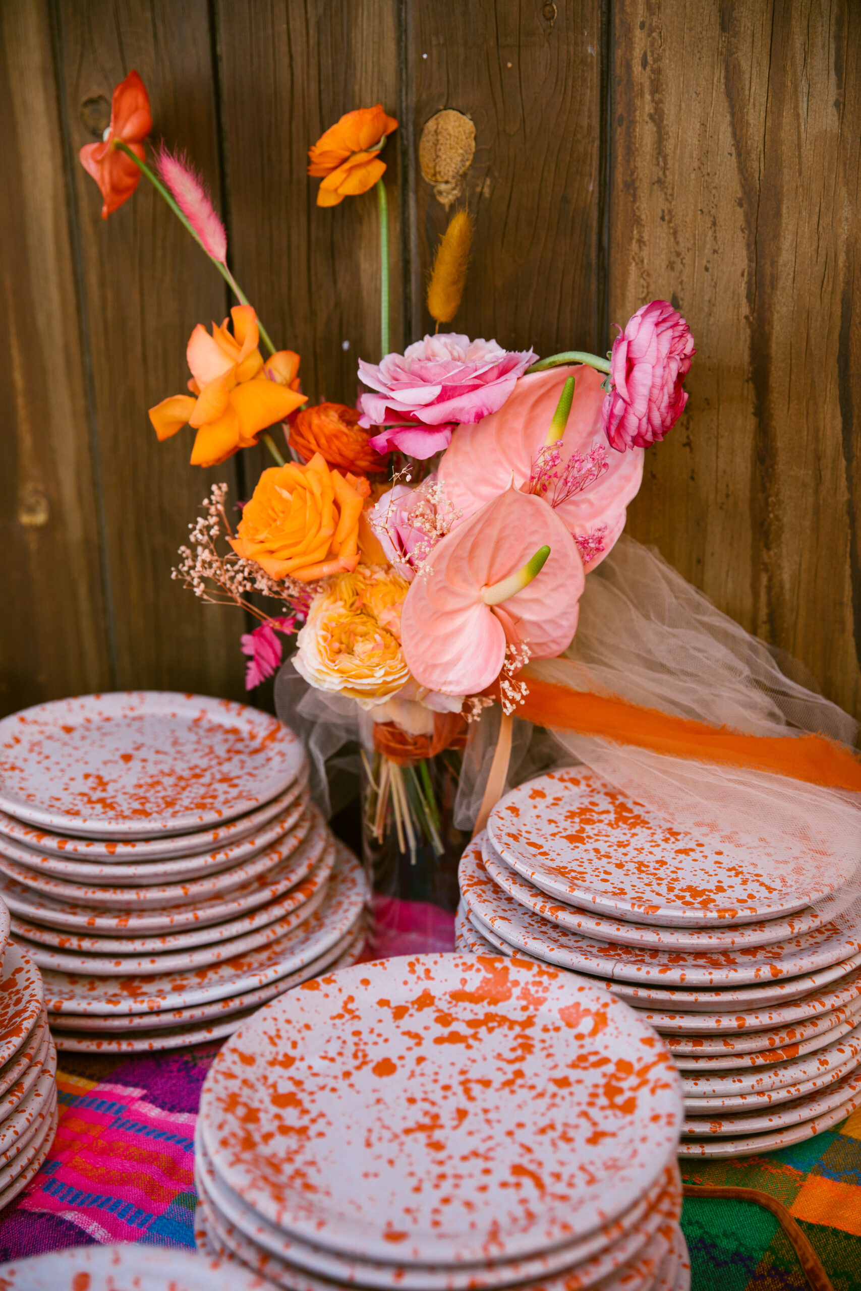 handmade mexican white stone plates with orange paint splatter. colorful pink orange peach and yellow bridal bouquet. colorful wedding dessert table with mexican blanket tablecloth. 