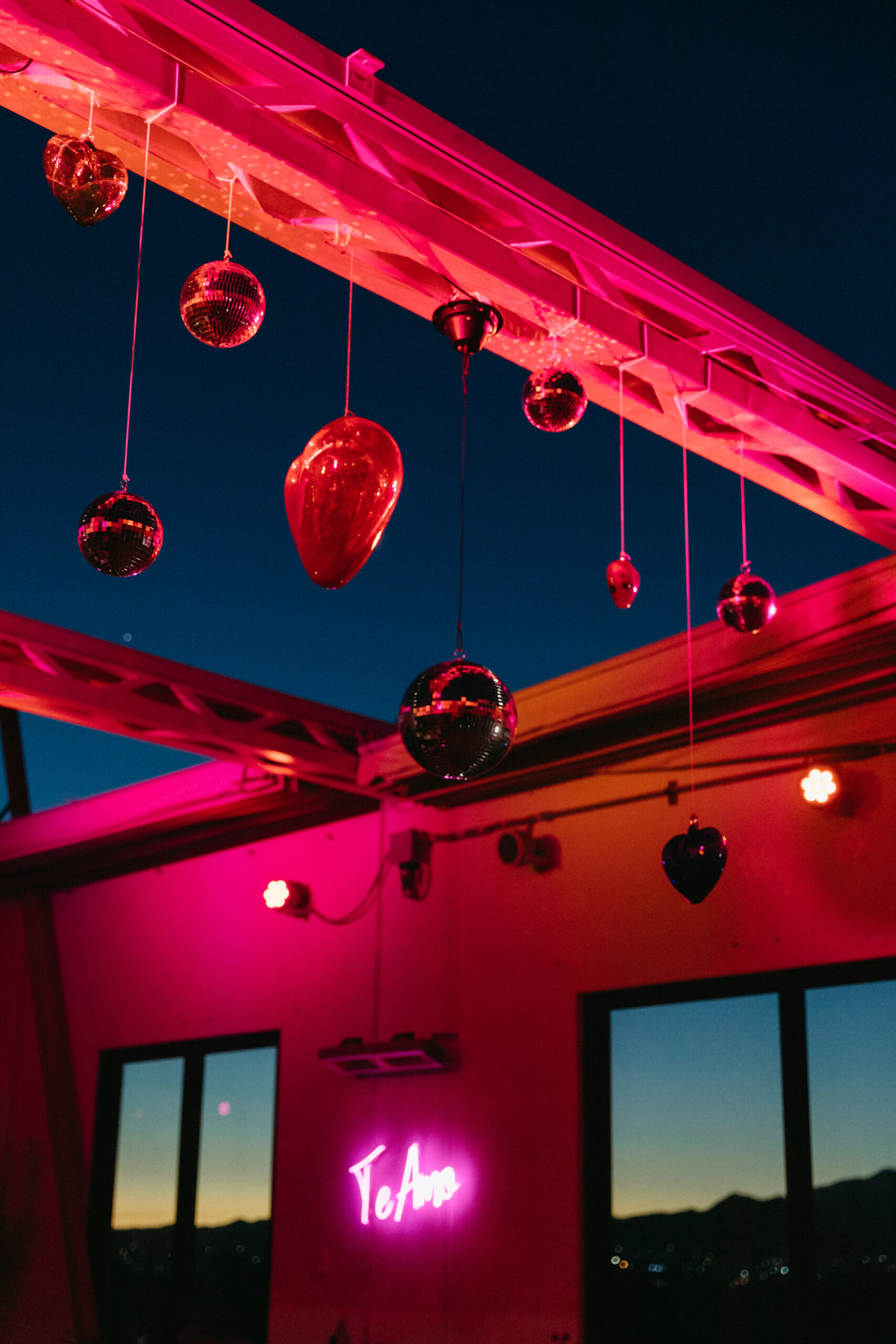 fuchsia pink moody lighting blown glass hearts and disco ball ceiling installation. hotel el ganzo open air dance party wedding te amo neon sign