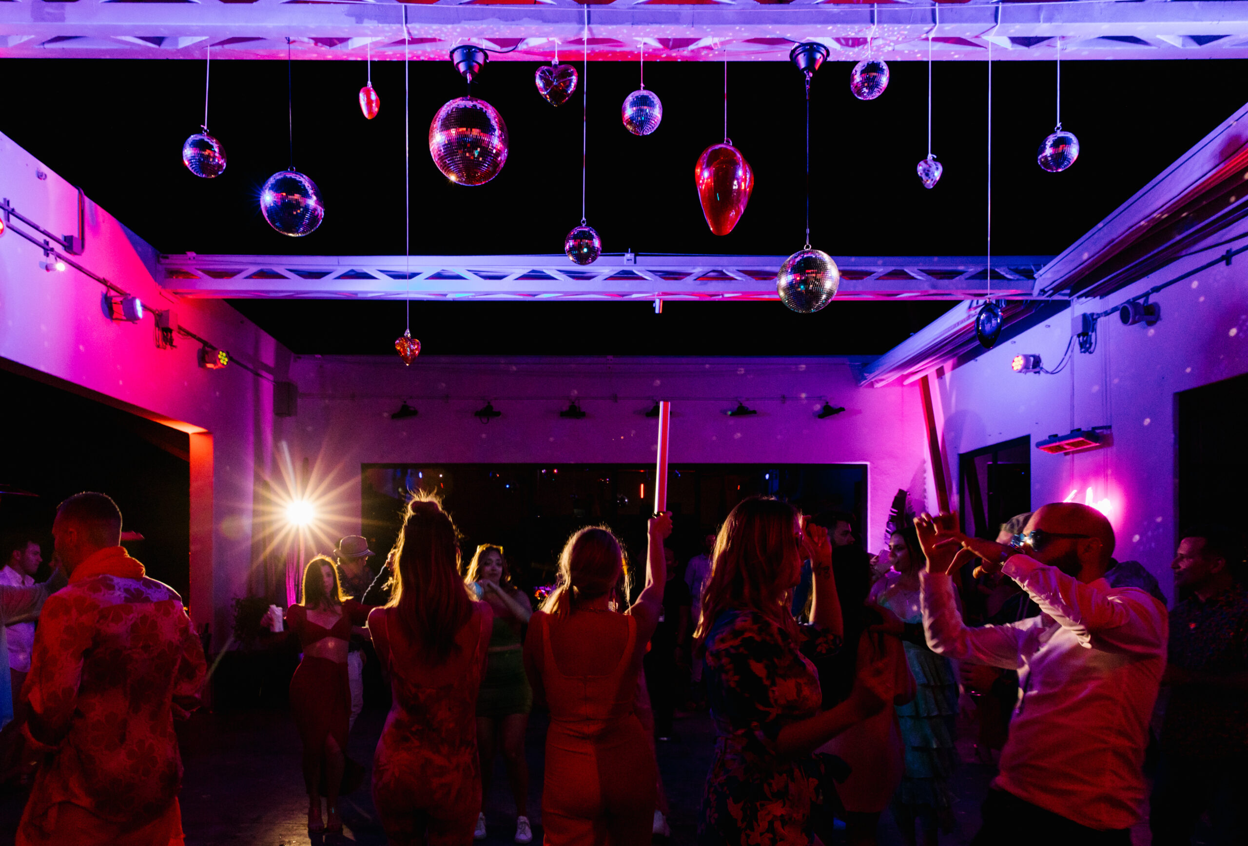 fuchsia red and purple pink moody lighting blown glass hearts and disco ball ceiling installation. hotel el ganzo open air dance party wedding te amo neon sign. 
hotel el ganzo DJ booth with aztec inspired mexican mural dj zebuel of sounds elevated
dance party