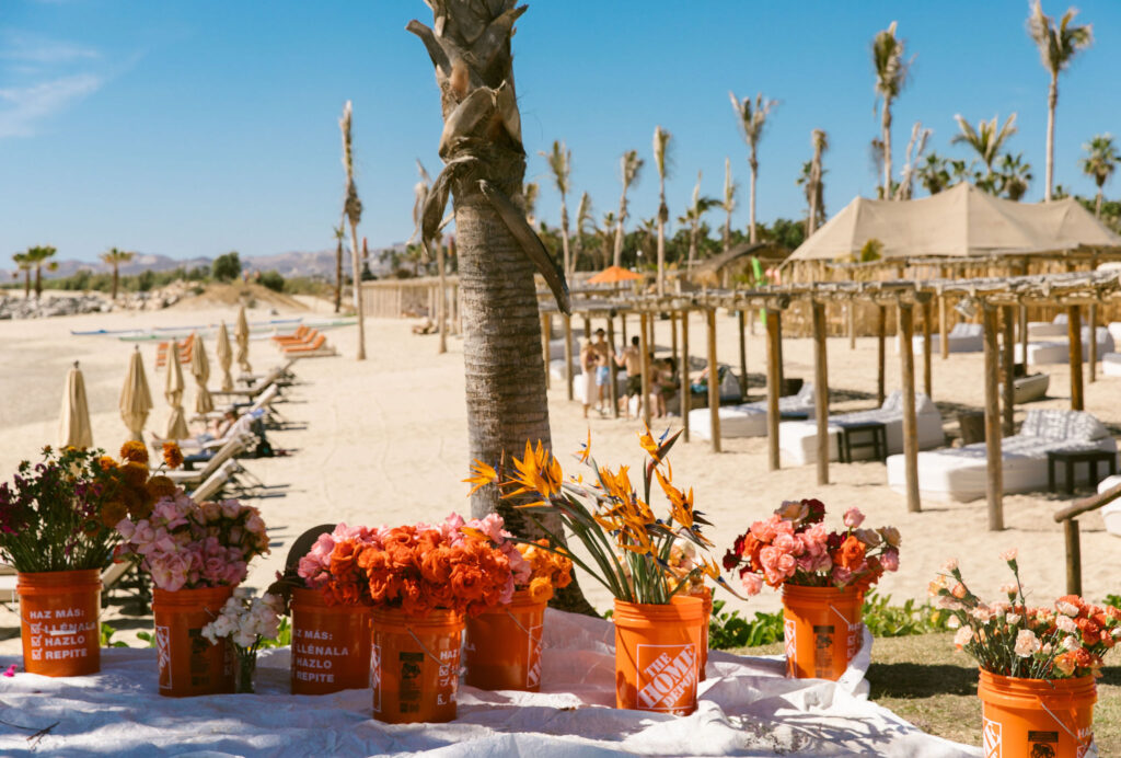 Orange home depot buckets filled with flowers on beach resort at el ganzo beach club in mexico. wedding ceremony floral behind the scenes prep