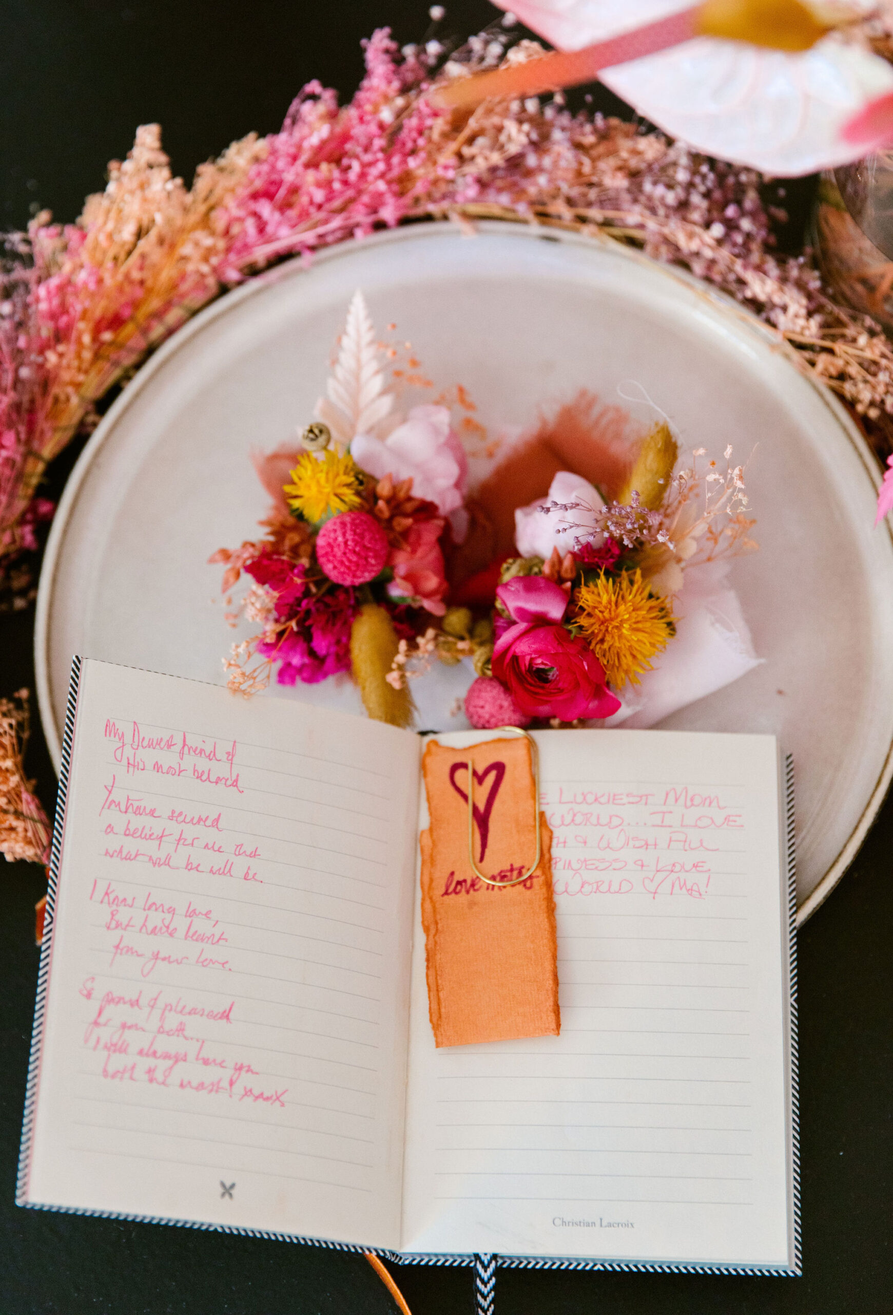 dried pink and yellow and orange floral crown with white stone plate on top and colorful wedding boutenir. wedding vows overlay overhead shot bright coral dyed bookmark