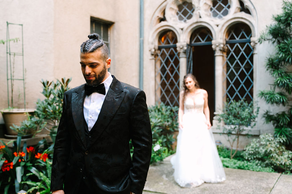 groom portraits groom wedding style man braids classy satin black suit with floral details and sparkly sequenced bowtie berkeley city club courtyard wedding first look simple classic airy wedding dress with tule and lace detailing