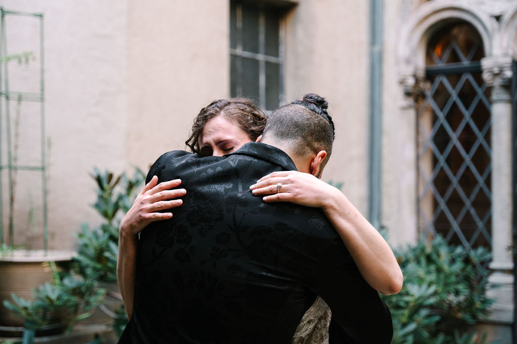 groom portraits groom wedding style man braids classy satin black suit with floral details and sparkly sequenced bowtie berkeley city club courtyard wedding first look simple classic airy wedding dress with tule and lace detailing couple crying holding each other candid in love