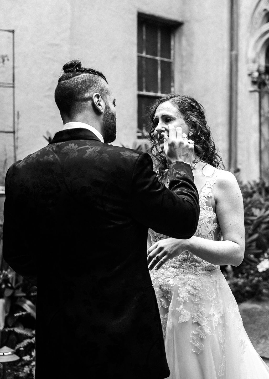 groom portraits groom wedding style man braids classy satin black suit with floral details and sparkly sequenced bowtie berkeley city club courtyard wedding first look simple classic airy wedding dress with tule and lace detailing black and white portrait candid emotional crying in love