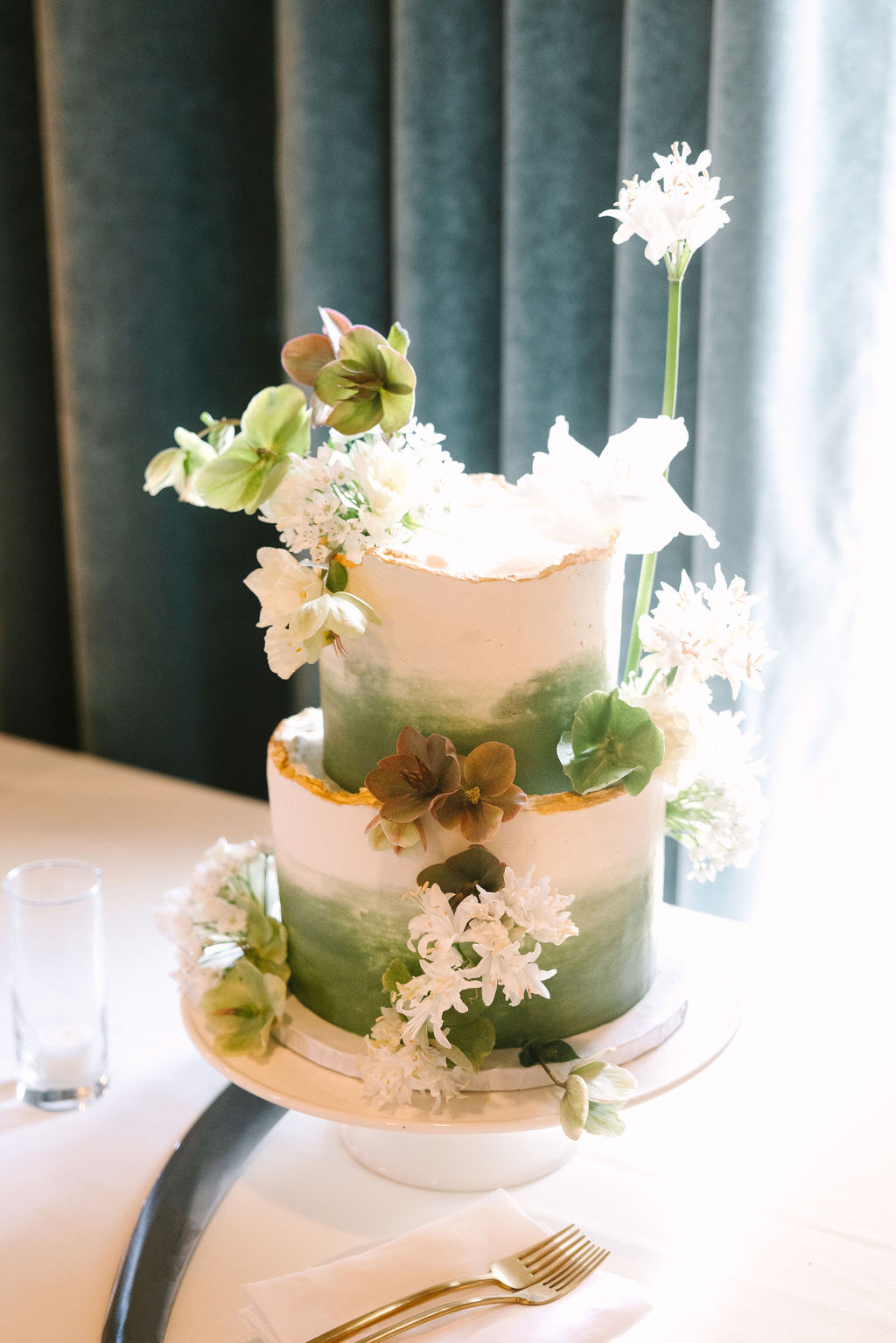 tiered wedding cake with green brush detailing and rough gold edges clean simple delicate white and green florals