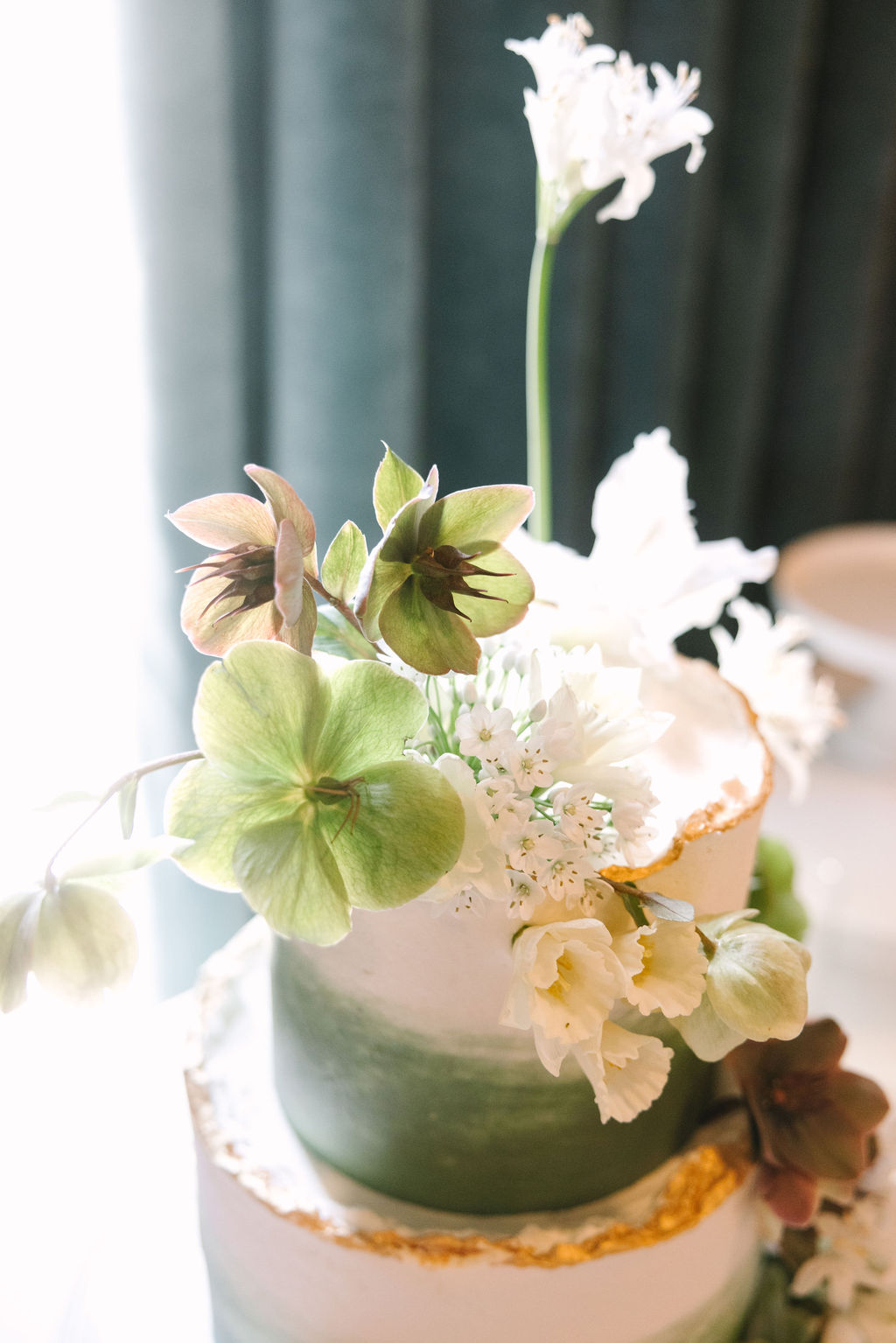 tiered wedding cake with green brush detailing and rough gold edges clean simple delicate white and green florals