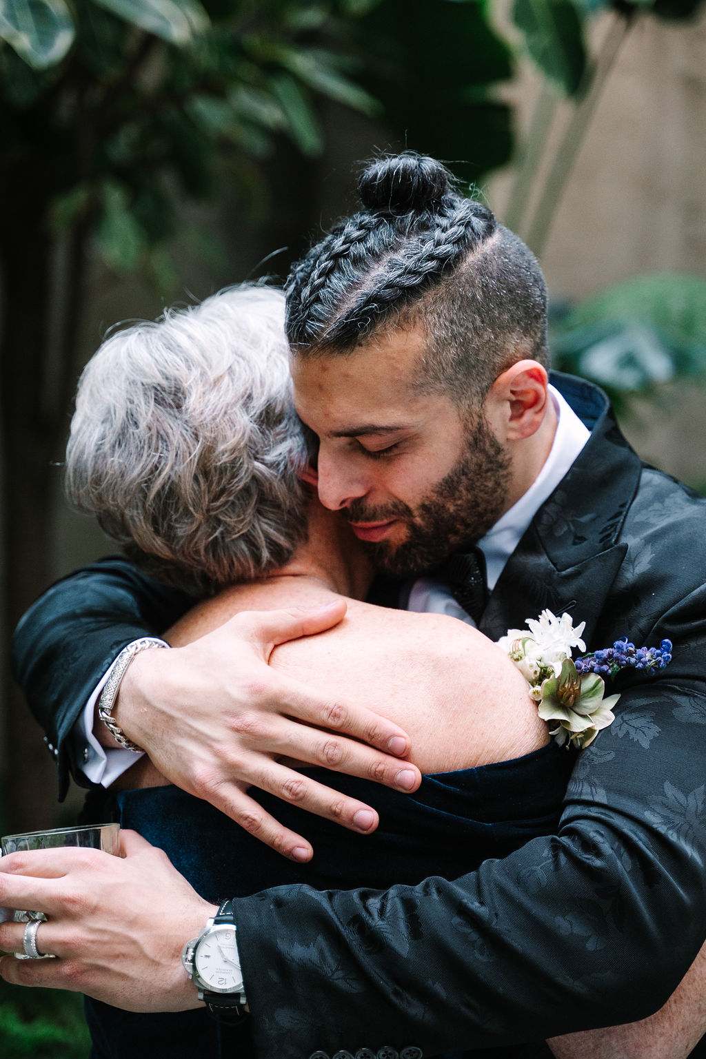 groom and mother hug after wedding ceremony emotional candid classy black satin suit with floral details delicate white florals with pop of sage green and blue
