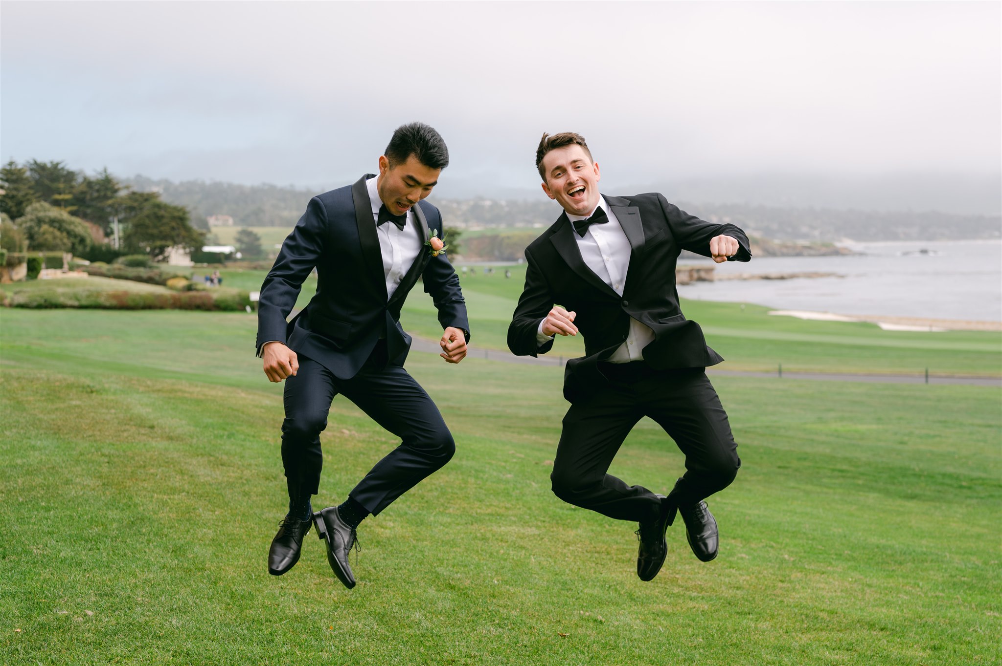 groom and groomsman best man jumping photo heels clicking navy blue suit with black details beach in back beachside wedding