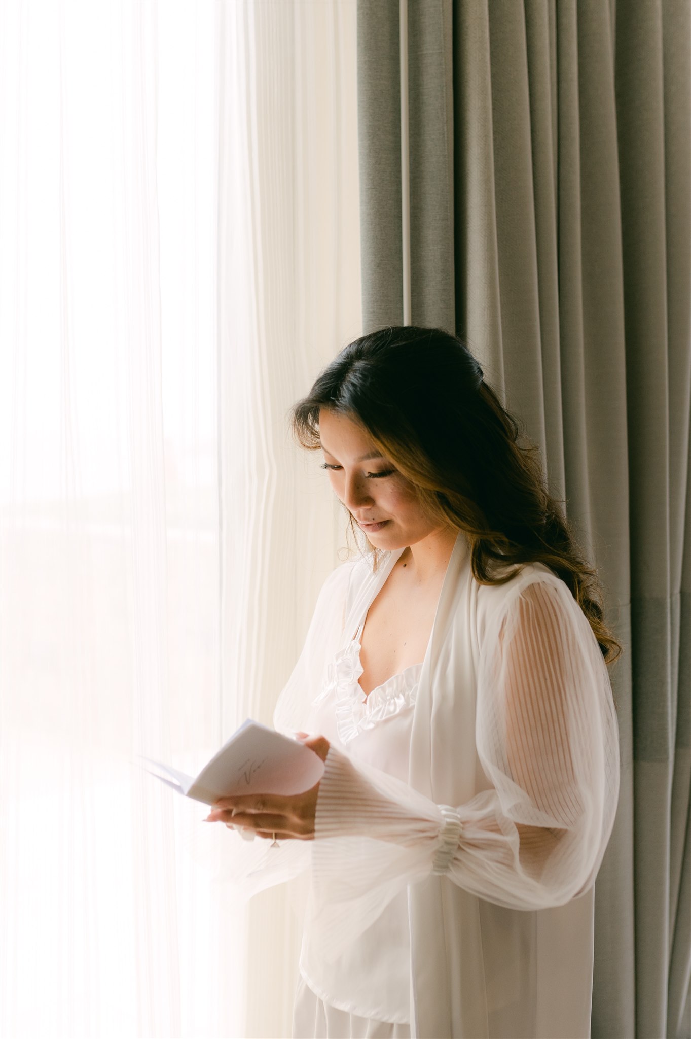 bride reading vow book next to open window dreamy ethereal bridal sheer robe and silk satin pajamas 