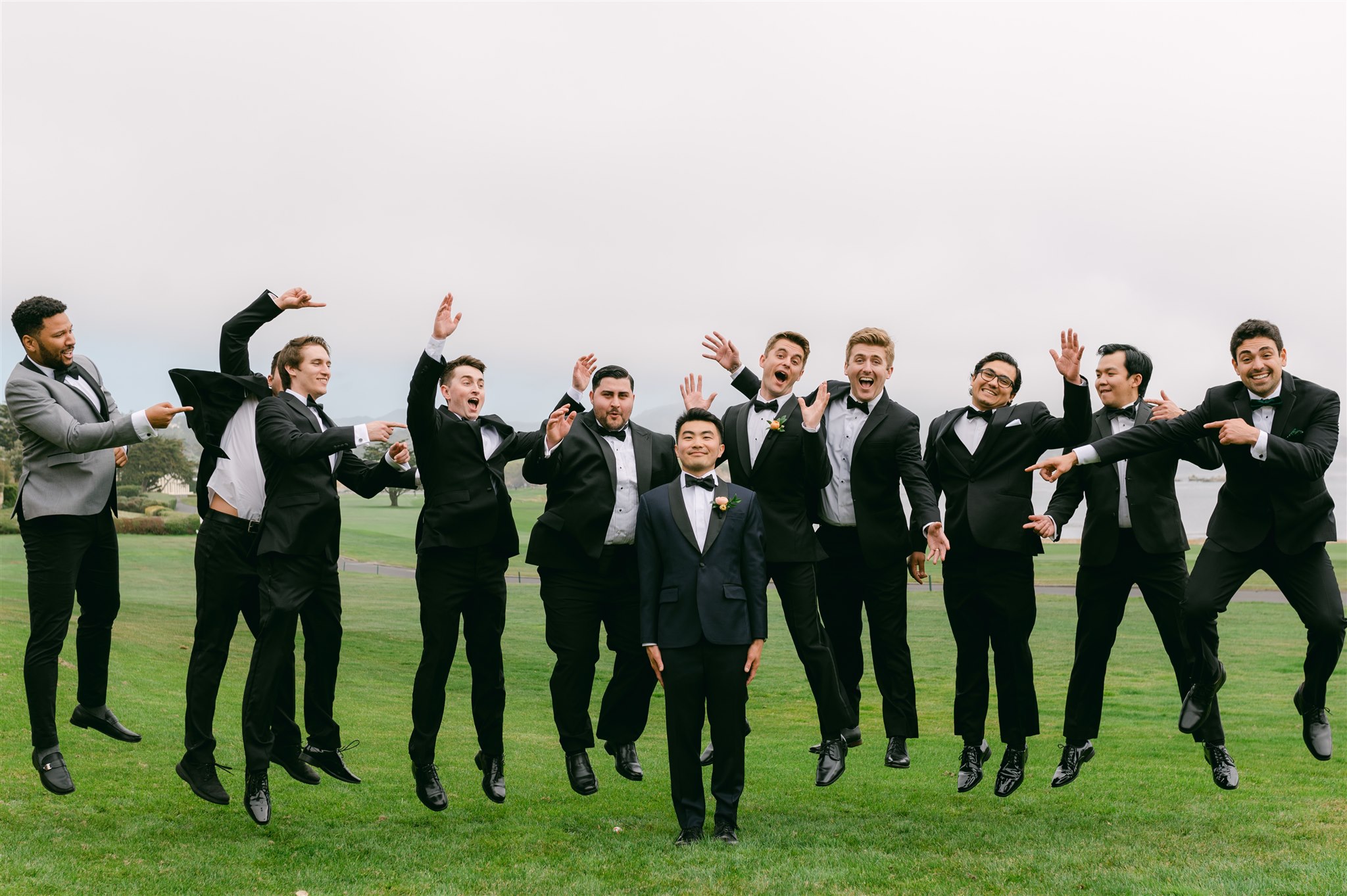 groom and groomsmen jumping portrait large bridal party black suits with black bowtie 