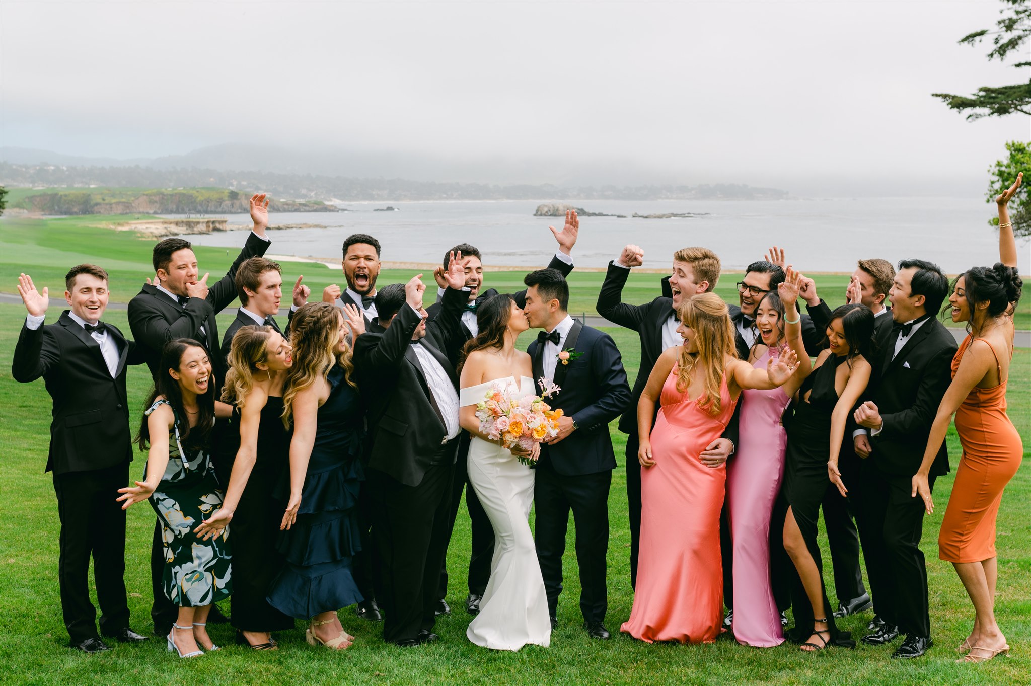 bridal party portraits unmatching bridesmaid dresses black suits with black bowtie beachside wedding bride and groom kiss peach pinks and white delicate floral wedding bouquet