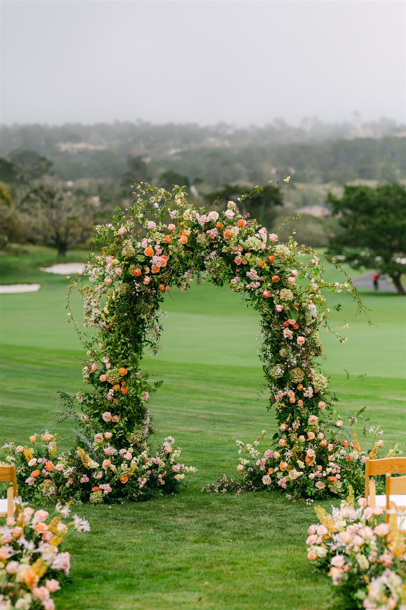 garden inspired wedding alter oranges pinks corals greens and white delicate florals carmel california wedding wooden chairs with white cushions