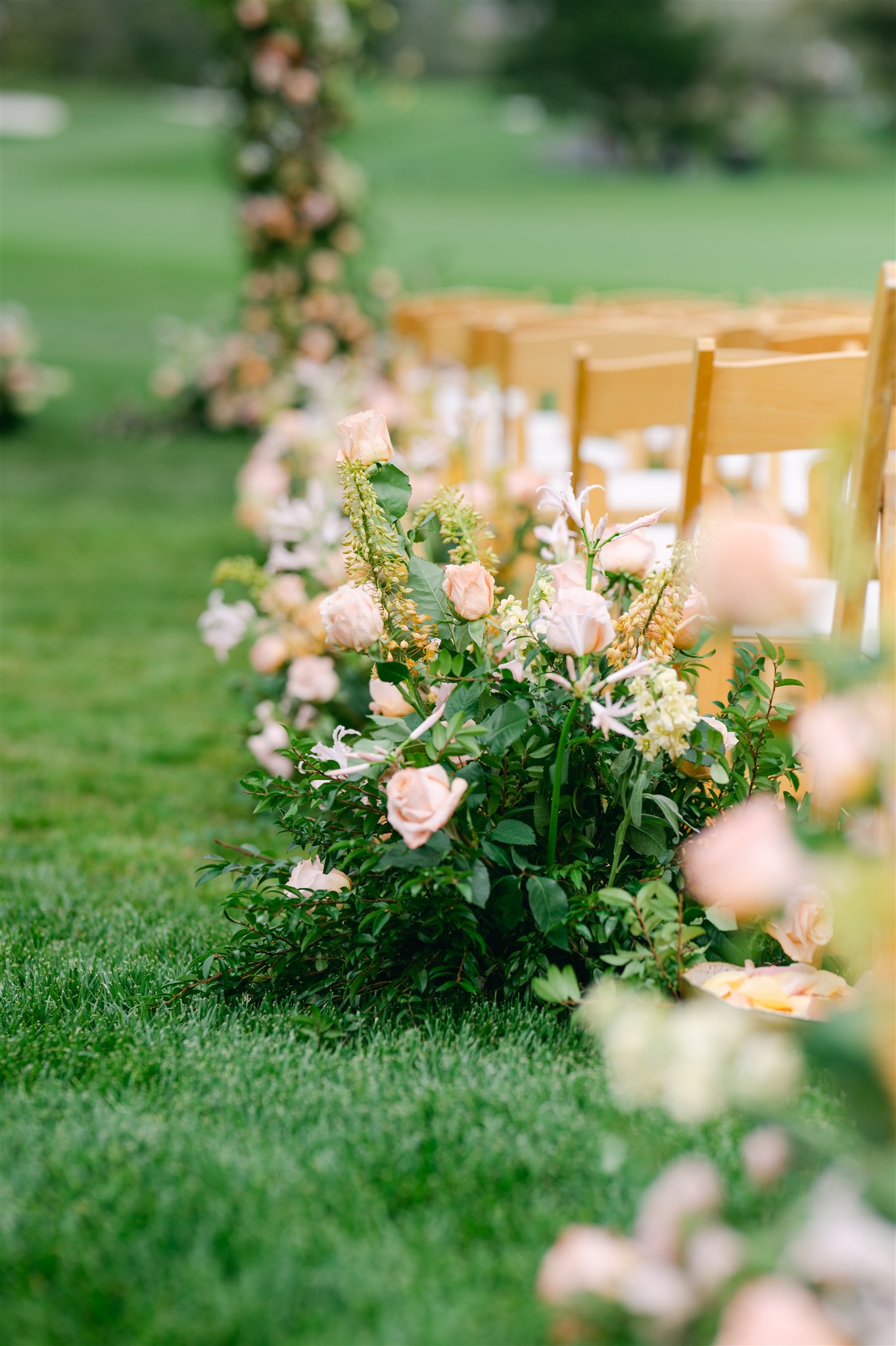 delicate pinks and orange florals and greens wooden chairs with white cushions wedding ceremony