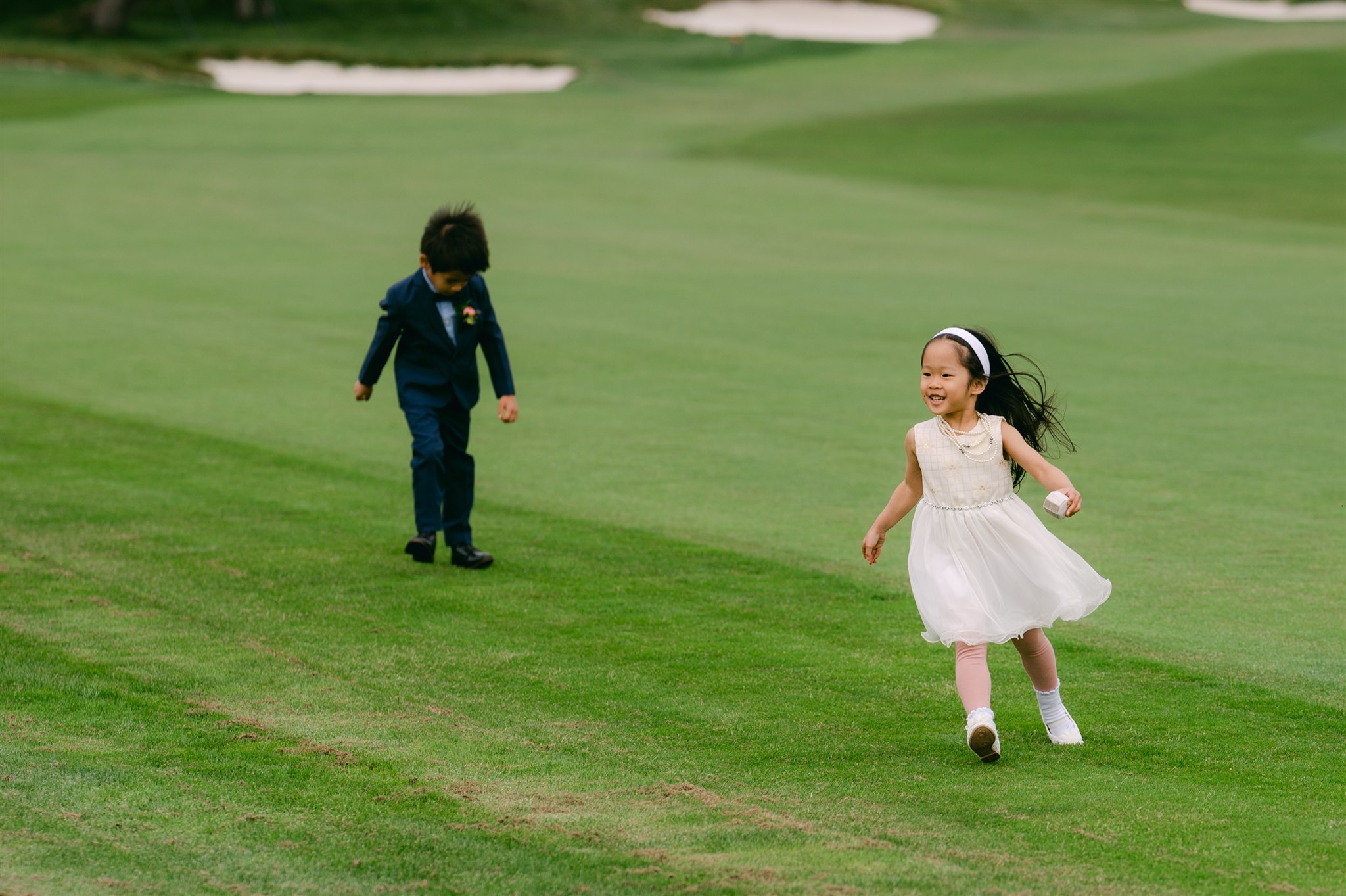 ring bearer and flower girl running in field golf course wedding party