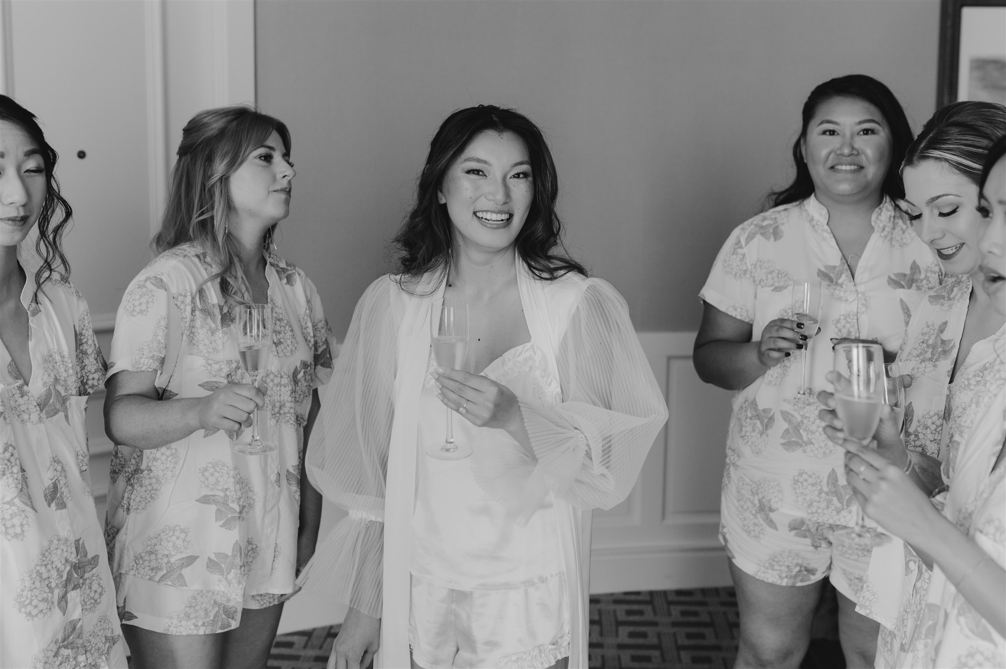 getting ready black and white portraits bridesmaids champagne matching floral pajama sets wedding day bride smiling