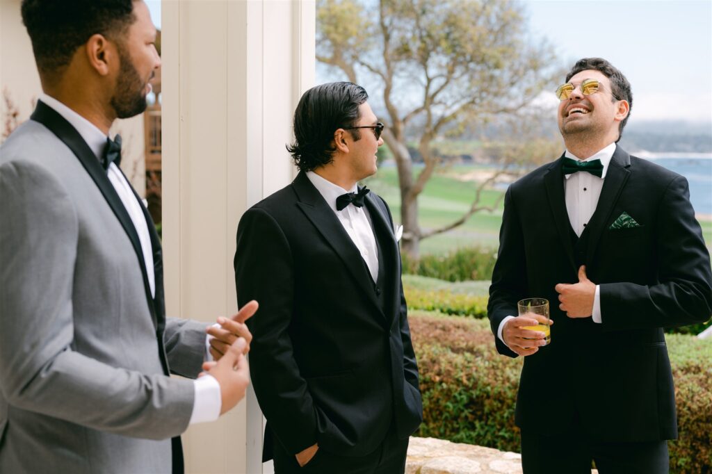 groomsmen wedding guests laughing gray suit with black details classic black suit with black bow tie beach views fairway one at pebble beach